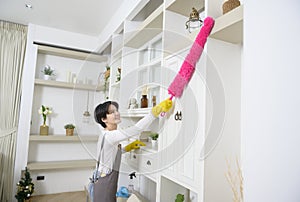 Happy Asian young woman sweeping sofa and furniture to cleaning house, healthy lifestyle concept