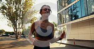 Happy athletic girl in sports summer uniform jogging in the morning. Beautiful rays of the sun shimmer on the camera