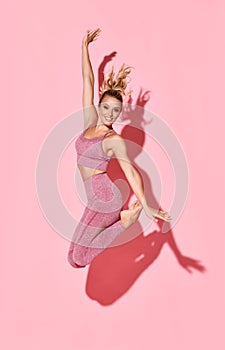 Happy athletic woman jumping in silhouette. Photo of sporty woman in fashionable pink sportswear on pink