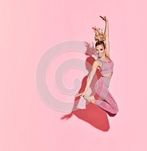 Happy athletic woman jumping in silhouette. Photo of sporty woman in fashionable pink sportswear on pink