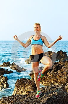 Happy athletic woman practicing yoga on the rocks by the sea