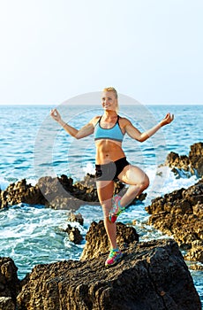 Happy athletic woman practicing yoga on the rocks by the sea