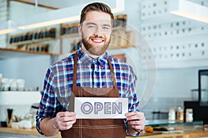 Happy attactive young barista holding open sign at coffee shop