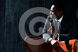 Happy attractive african american businessman in suit leans on chair and shows okay sign