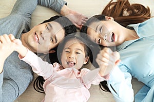 Happy attractive asian family with mom, dad and little cute young daughter or elementary kids holding hands together lying on