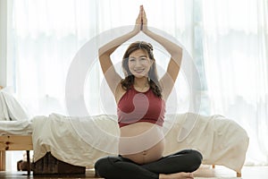 Happy Attractive Asian Pregnant woman practice yoga lotus pose to meditation smile with big belly after wake up in the morning Fee