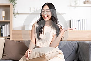 Happy attractive asian young woman smile and open hand palm to copy space at home. Cheerful pretty girl wear casual dress open