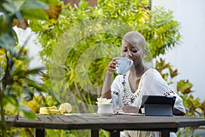 Happy attractive black afro American woman working with tablet outdoors at cafe relaxed drinking tea or coffee in digital nomad su