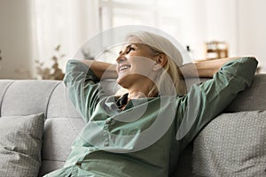 Happy attractive blonde senior woman relaxing on comfortable cozy sofa