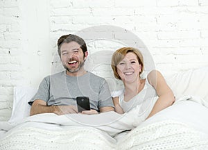 Happy attractive couple in bed using mobile phone smiling watching together internet app