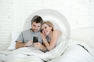 happy attractive couple in bed using mobile phone smiling watching together internet app