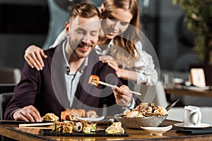 Happy attractive couple having dinner and eating tasty sushi rolls