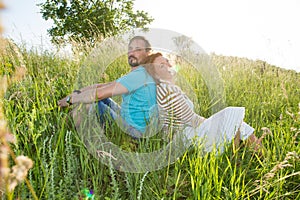 Happy attractive couple sitting together at outdoors picnic. Couple on grass in summer forest in green grass.