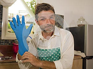 Happy and attractive man enjoying dishwashing at home kitchen in apron putting washing rubber glove smiling satisfied doing