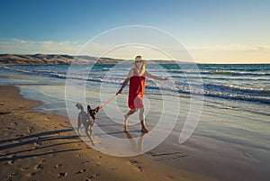 Happy attractive mature woman with her pet walking on friendly dog beach at sunset