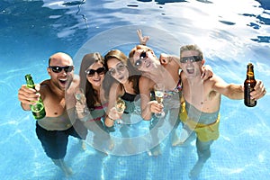 Happy attractive men and women in bikini having bath at hotel resort swimming pool drinking beer