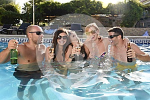 Happy attractive men and women in bikini having bath at hotel resort swimming pool drinking beer