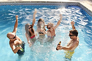 Happy attractive men and women in bikini having bath at hotel resort swimming pool drinking beer