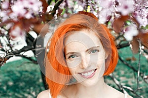 Happy attractive red-haired woman with freckles standing outdoors in spring cherry blossom