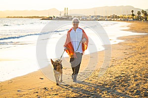 Happy attractive senior woman with her german shepard dog walking on the beach at autumn sunset