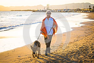 Happy attractive senior woman with her german shepard dog walking on the beach at autumn sunset