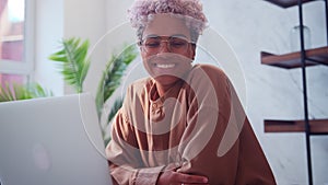 Happy attractive young afro american woman sitting at laptop smiling at camera.