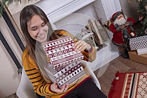 Happy attractive young Asian woman opening Christmas gifts near fireplace and christmas tree