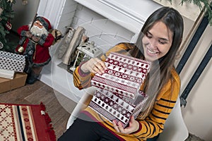 Happy attractive young Asian woman opening Christmas gifts near fireplace and christmas tree