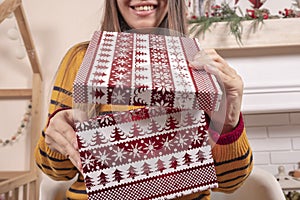 Happy attractive young Asian woman opening Christmas gifts near fireplace and christmas tree