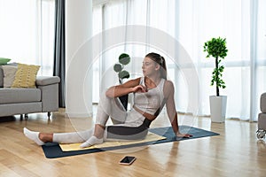 Happy attractive young business woman in active sport wear sitting on stretching muscles at her apartment after or before the work