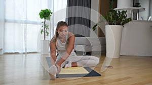 Happy attractive young business woman in active sport wear sitting on stretching muscles at her apartment after or before the work