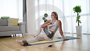 Happy attractive young business woman in active sport wear sitting on stretching muscles at her apartment after or before the work