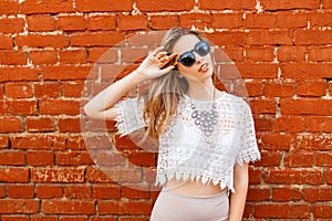 Happy attractive young hipster woman in sunglasses in a white lace blouse with a beautiful shiny necklace in a skirt posing near a