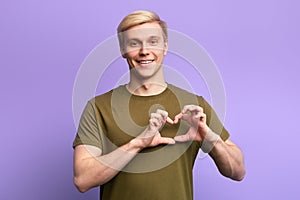 Happy attractive young man, holding hands in heart gesture ,