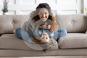 Happy attractive young mom tickling little preschool daughter.