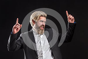 Happy attrative young businessman in black suit listening music with earphones and dancing over gray background.