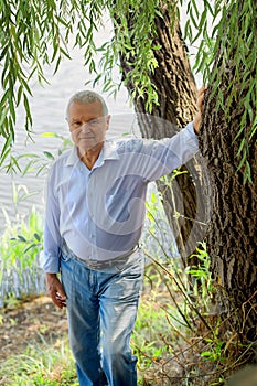 Happy Ñaucasian older mature gray-haired man 60 plus in white shirt and blue jeans by the lake. Retired lifestyle. Rest and