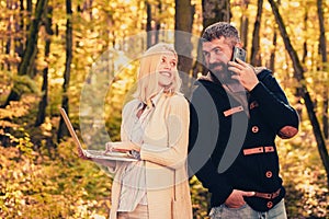 Happy autumn couple. Business couple - woman browsing Internet on a notebook, man using mobile phone outdoors. Autumn