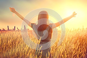 Happy autumn woman raising hands over sunset sky, enjoying life and nature. Beauty female on field looking on sun