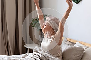 Happy awakened aged woman stretching after night sleeping photo