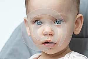 A happy baby with blue eyes is sitting in a high chair, smiling at the camera