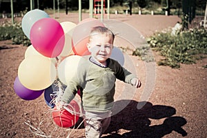 Happy baby boy with balloons plays on playground. Smile