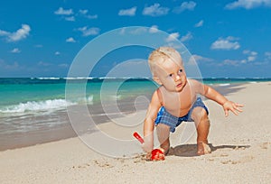 Happy baby boy digging sand on sunny tropical beach