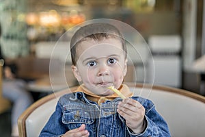 A happy baby boy eats French fries. fast food. European.