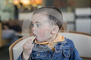 A happy baby boy eats French fries. fast food. European.