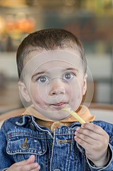 A happy baby boy eats French fries. fast food. European.