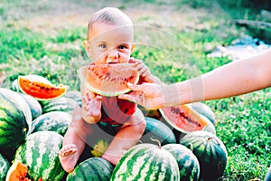 Happy baby boy in funny costume sitting and eating slice of watermelon