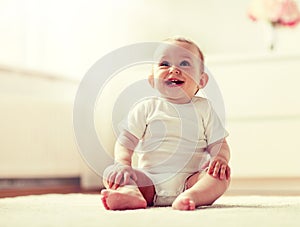 Happy baby boy or girl sitting on floor at home