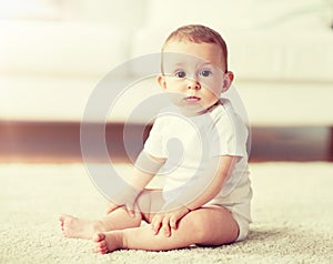 Happy baby boy or girl sitting on floor at home