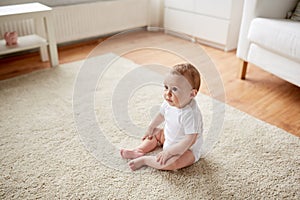 Happy baby boy or girl sitting on floor at home